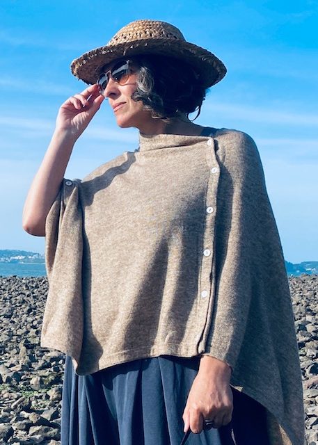 A woman on the beach wearing a fawn coloured Fairtrade Cashmere Poncho